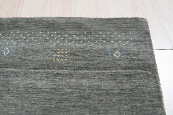 Nubby grayish-green rug with small white, yellow, and blue geometric patterns rests on light wood planks.
