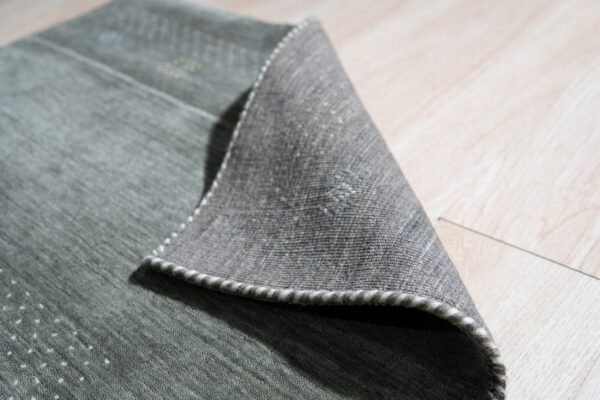 A textured green rug with white accents is folded over, revealing the woven back and striped edge binding.