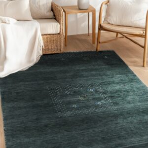 A striated dark teal rug with a dotted pattern lies on wood flooring surrounded by wicker furniture.