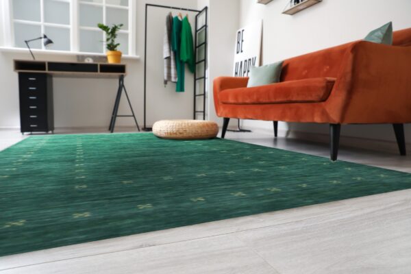 A green rug with repeating yellow motifs covers light flooring in a room with an orange velvet sofa.