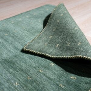 Textured green rug with yellow cross patterns folded back on light wood plank flooring.