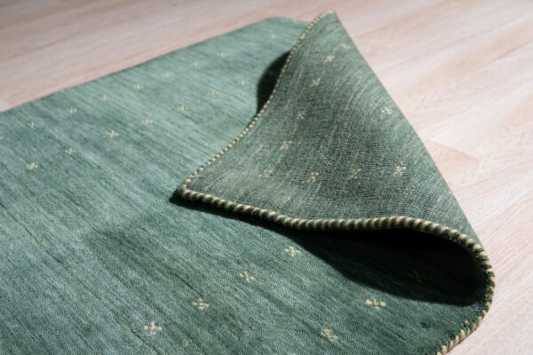 Textured green rug with yellow cross patterns folded back on light wood plank flooring.