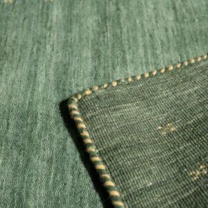 Close-up of a green rug showing the low pile surface, striped binding, and darker woven backing.