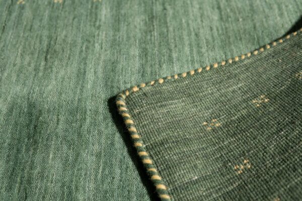 Close-up of a green rug showing the low pile surface, striped binding, and darker woven backing.