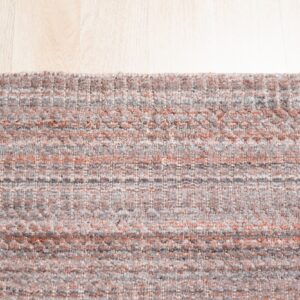 Textured gray and rust rug with a linear pattern rests on light blonde wood flooring.