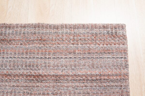 Textured gray and rust rug with a linear pattern rests on light blonde wood flooring.