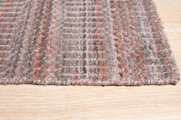 Textured high pile rug in heathered gray and rust orange with a geometric grid pattern on light wood.