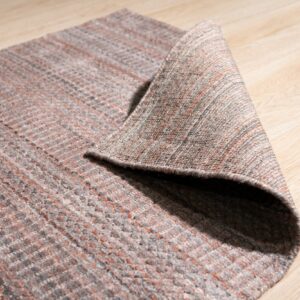 A low-pile gray and rust textured rug is folded over on light blonde wood flooring.