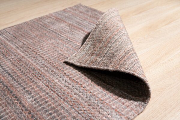 A low-pile gray and rust textured rug is folded over on light blonde wood flooring.