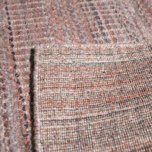 Close-up showing a rug's variegated gray and rust color surface next to its tightly woven backing.