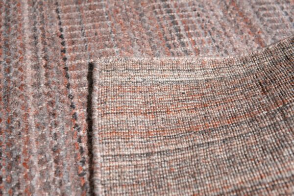 Close-up showing a rug's variegated gray and rust color surface next to its tightly woven backing.