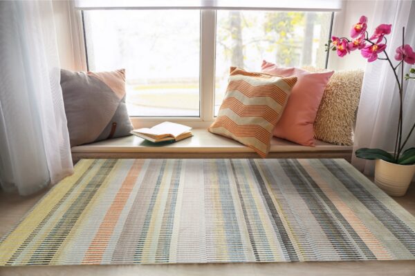 Multicolor striped rug in yellow, orange, blue, and gray sits under a sunny window seat.