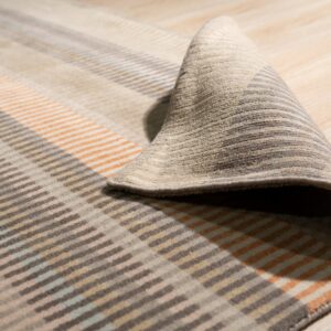 A low-pile rug with geometric stripe patterns in brown, tan, orange, and light blue is curled on light wood flooring.