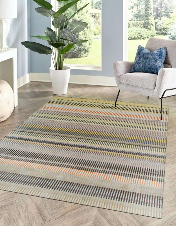 Multi-color dash stripe rug on herringbone flooring next to a grey chair and large window.