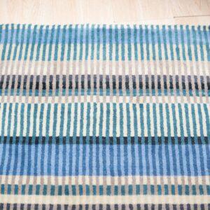 Close-up of a low-pile rug with blue, teal, gray, and cream vertical stripes over light wood flooring.