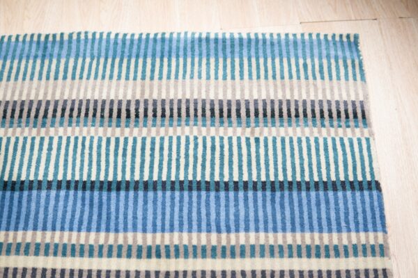 Close-up of a low-pile rug with blue, teal, gray, and cream vertical stripes over light wood flooring.