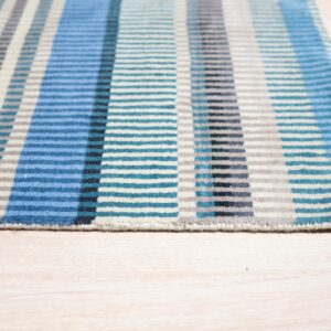 Geometric striped low pile rug in blue, teal, gray, and cream on a light wood floor.