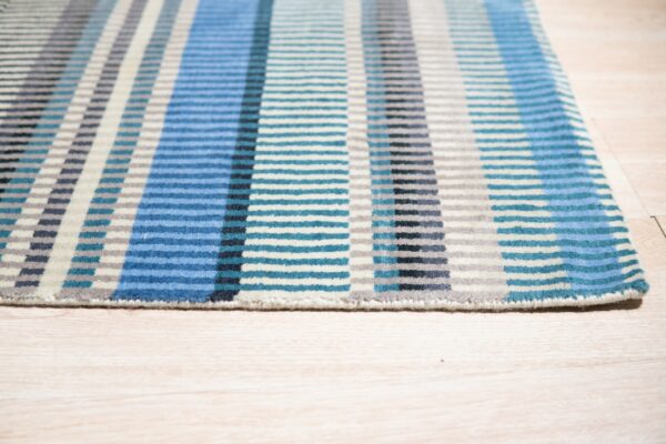 Geometric striped low pile rug in blue, teal, gray, and cream on a light wood floor.