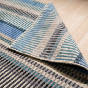 A blue, teal, gray, and beige striped rug is partially folded on light wood flooring.