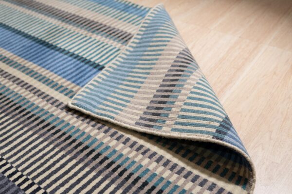 A blue, teal, gray, and beige striped rug is partially folded on light wood flooring.