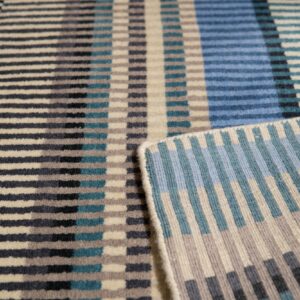 Geometric rug in blue, teal, gray, and cream with short pile and a flatwoven edge.
