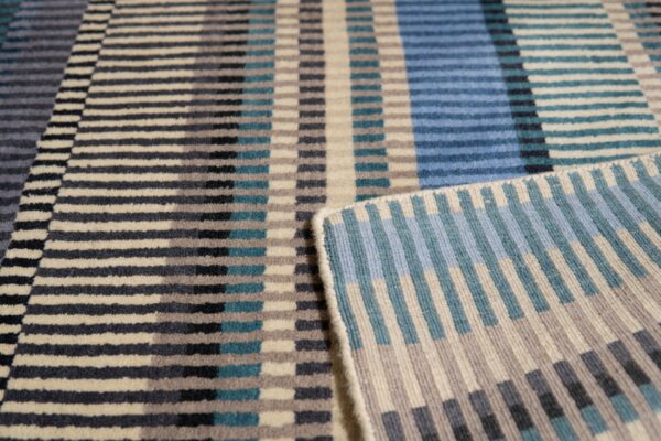 Geometric rug in blue, teal, gray, and cream with short pile and a flatwoven edge.