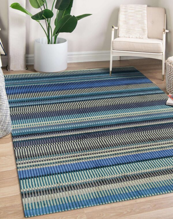 A low-pile blue, teal, and beige striped rug sits on a wood floor near a white chair and houseplant.