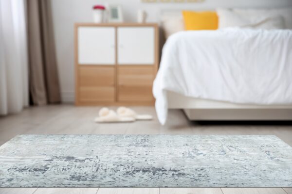 Distressed gray and white abstract rug on a light floor, with a blurred bed in the background.