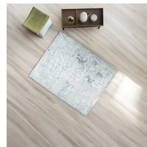 Distressed light gray rug displayed on pale wood flooring, next to an olive stool and a decorative tray.