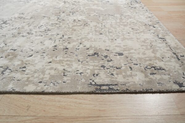 A beige and gray abstract rug with a textured high-low pile rests on light wooden floorboards.