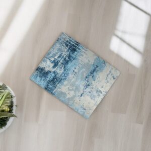 Abstract blue and gray rug placed diagonally on light wood floors with natural light and window shadows.