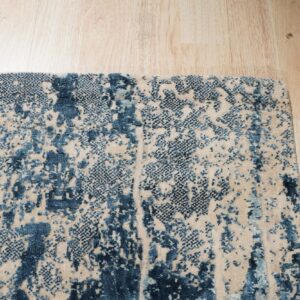 Abstract high-low pile rug in blue and beige displayed on light wood plank flooring.