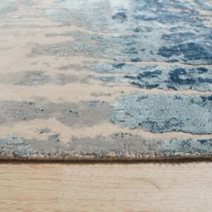 Abstract rug in shades of blue, gray, and beige showing varied pile texture on wood floor.