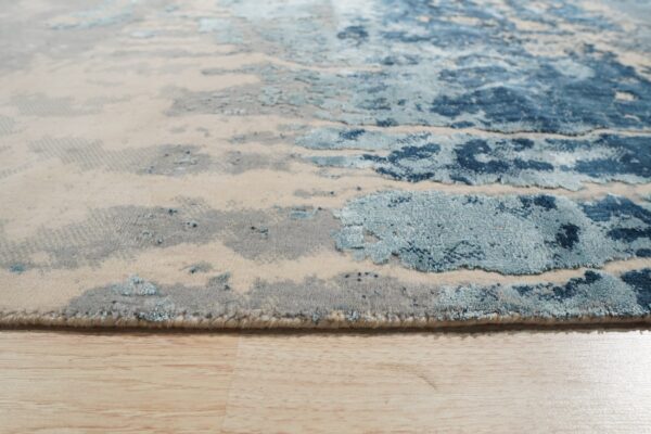 Abstract rug in shades of blue, gray, and beige showing varied pile texture on wood floor.