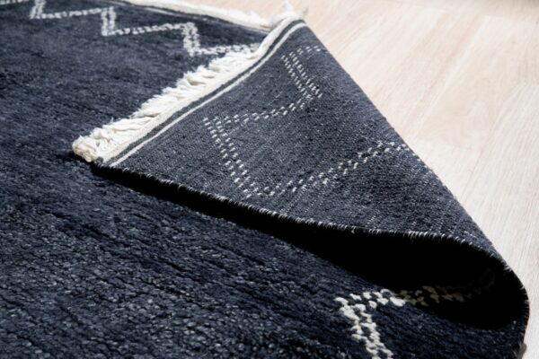 High-pile navy rug with white geometric designs folded over, showing its flat patterned backing on light wood.