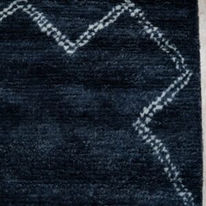 High pile navy rug with a dotted white chevron pattern and fringe shown on light blonde wood flooring.