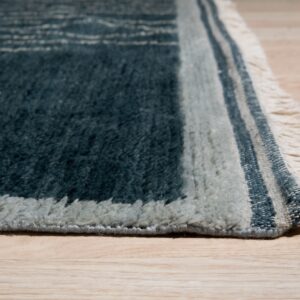 High-pile rug in teal and light gray colors with fringed edges on light wooden flooring.