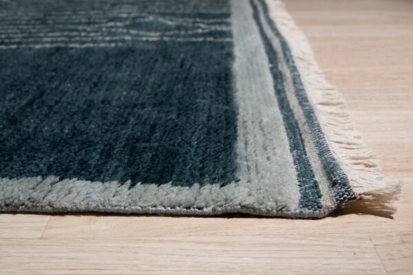 High-pile rug in teal and light gray colors with fringed edges on light wooden flooring.