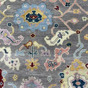 A close-up view of a textured gray rug with a colorful blue, pink, and yellow traditional floral pattern.