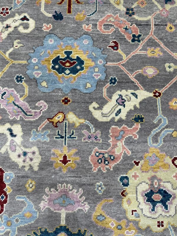 A close-up view of a textured gray rug with a colorful blue, pink, and yellow traditional floral pattern.