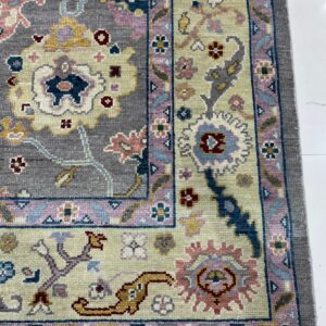 A textured rug displaying a gray and beige floral pattern with pastel pink and blue borders on white tile.