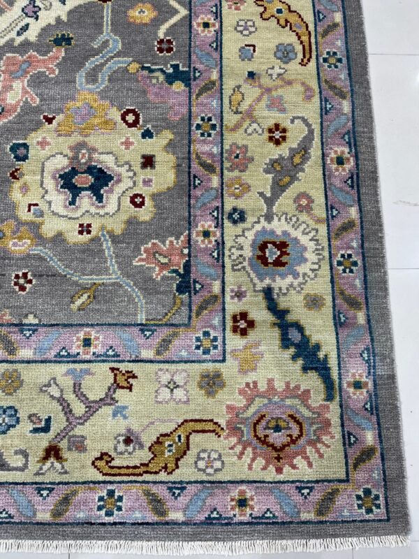 A textured rug displaying a gray and beige floral pattern with pastel pink and blue borders on white tile.