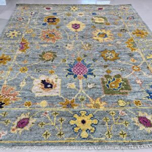 A textured blue rug with colorful traditional floral patterns in yellow, magenta, and green on white tiled flooring.
