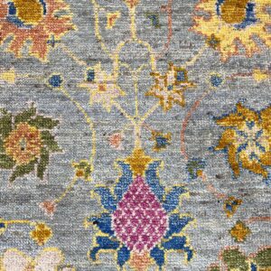 Detail of a textured rug with a blue-gray background and colorful floral motifs in gold, blue, and magenta.