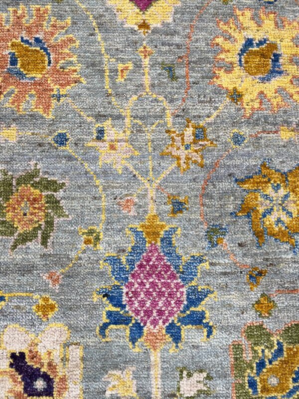 Detail of a textured rug with a blue-gray background and colorful floral motifs in gold, blue, and magenta.