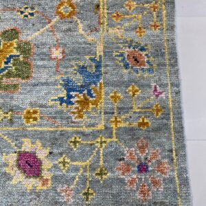 Textured blue-gray rug featuring traditional floral patterns in yellow, magenta, and blue accents rests on a white tile floor.