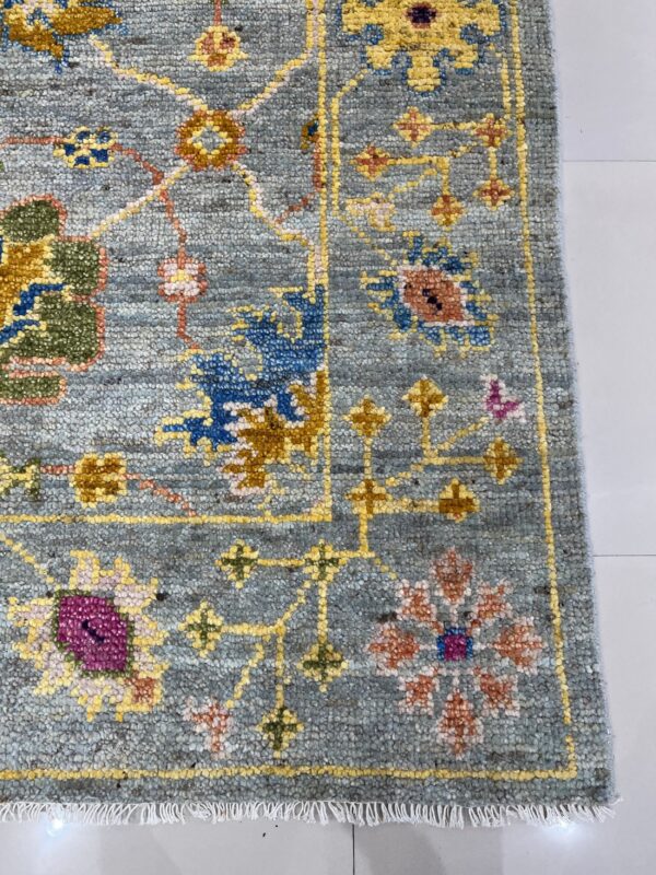 Textured blue-gray rug featuring traditional floral patterns in yellow, magenta, and blue accents rests on a white tile floor.