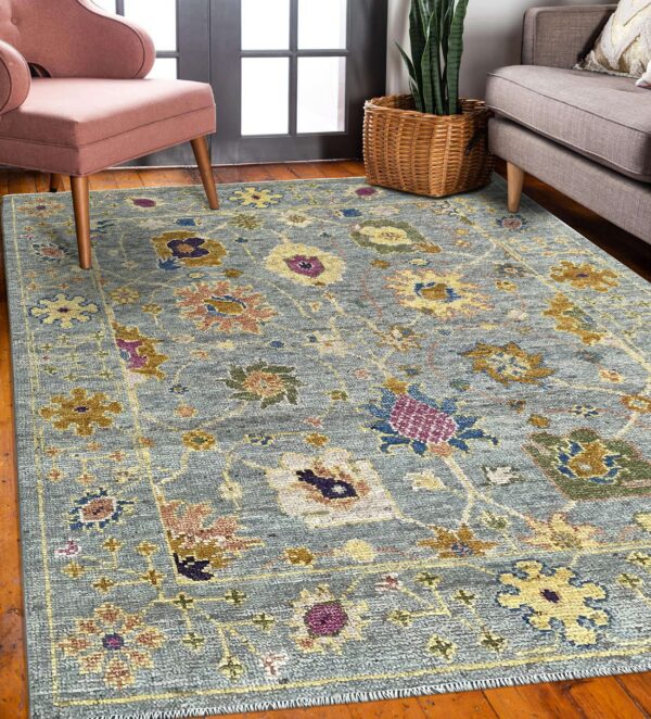 Traditional blue-gray rug with multicolor florals anchors a room featuring a pink chair and wood flooring.