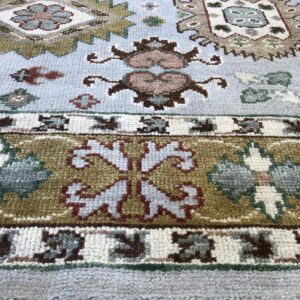 Light blue traditional rug with olive and rust geometric patterns resting on light wood flooring.