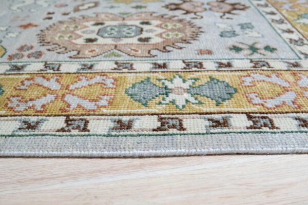 Ornate light blue rug with gold, cream, and teal borders rests on pale wooden floorboards.